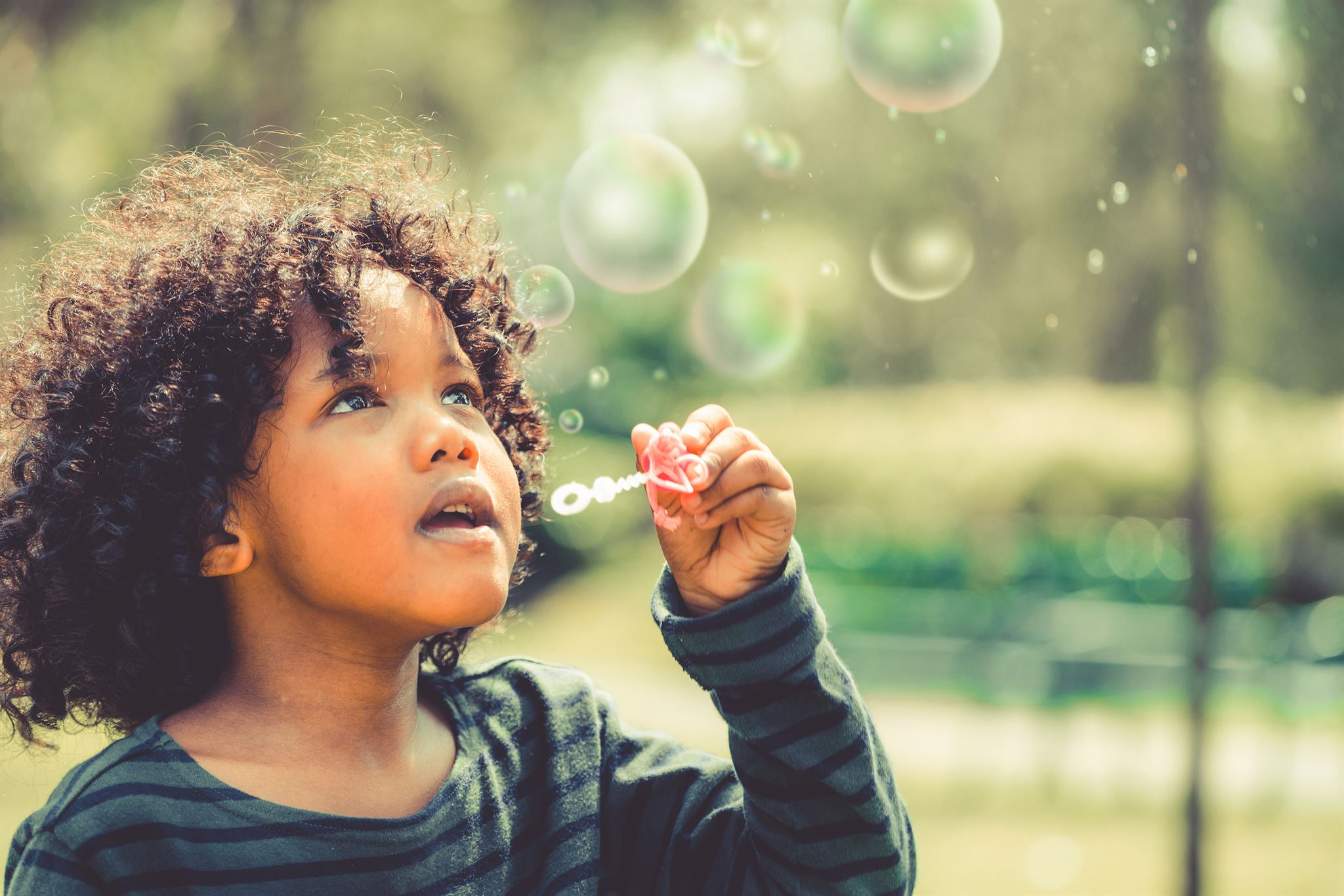 Child-holding-bubble-wand-near-mouth-and-looking-upwards-at-bubbles-of-various-sizes